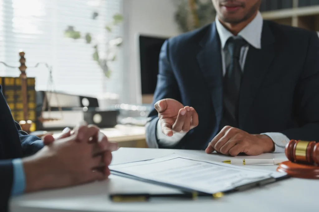 Attorney in a suit reviewing paperwork with a client across a desk, with a gavel and scales of justice nearby